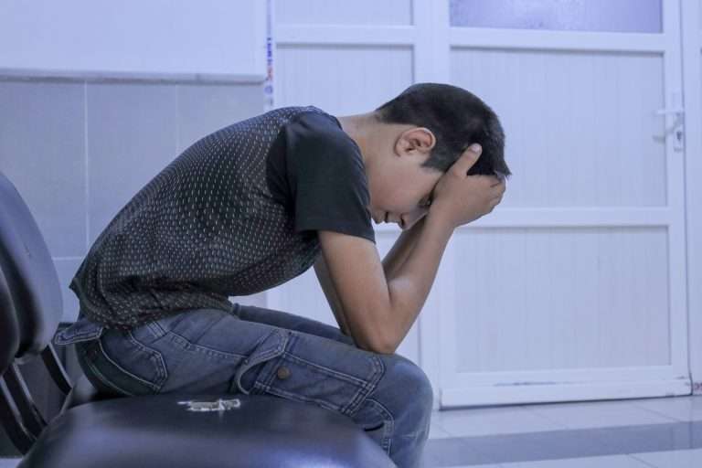 A man sitting on a chair with his head in his hands. A child feels lonely and holds his head in pain.